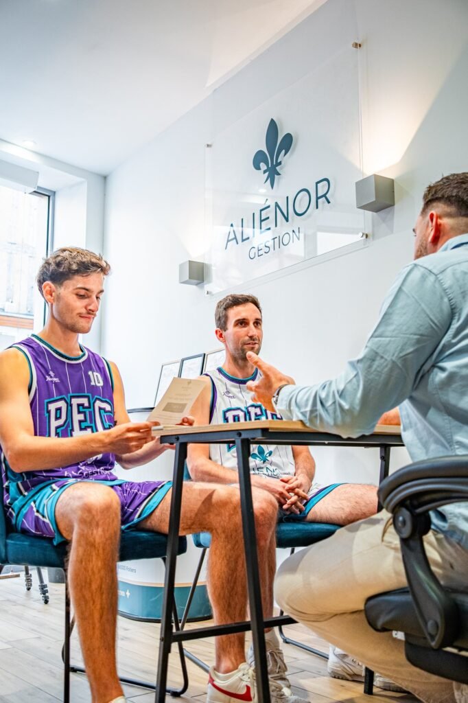 Deux joueurs du PEC Basket Poitiers assis au bureau de l'agence Aliénor Gestion avec Thomas Bris