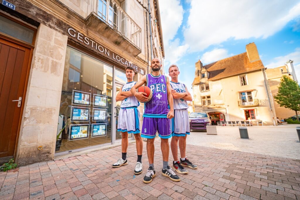 Trois joueurs du PEC Basket Poitiers portant les nouveaux maillots violets floqués Aliénor Gestion, devant l'agence